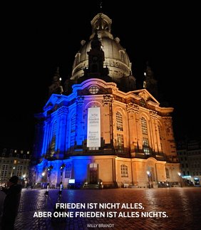 Dresdener Frauenkirche in den blau-gelbem Licht mit Zitat von Willy Brandt - Frieden ist nicht alles, aber ohne Frieden ist alles nichts.