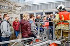 Besuch des Masterstudiengangs Brandschutz bei der Feuerwehr Dresden - eine Gruppe Studierender auf der linken Seite des Bildes, auf der rechten Seite steht ein Herr von der Feuerwehr in entsprechender Kleidung